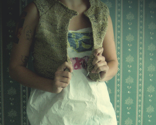 a short brown vest over a white and dark green dress, both made from plastic grocery bags