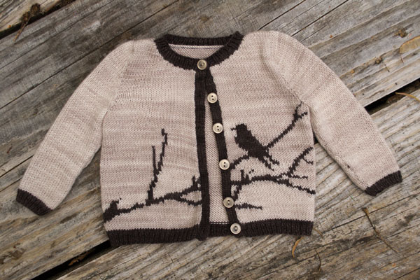 a cream colored knit baby sweater with a dark brown sillhouette of a bird on a branch in intarsia