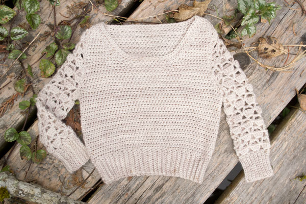 a cream colored crocheted baby sweater with lace sleaves