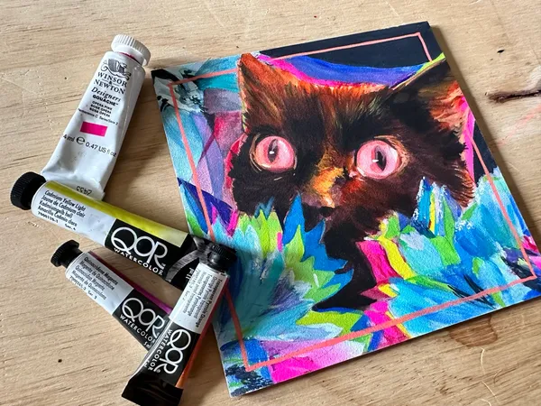 Watercolor cat next to QOR watercolor tubes and an opera pink Winsor & Newton gouache tube